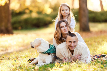Fototapeta premium Happy family is having fun with dog labrador are lying on green grass in park.