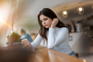 young beautiful sad woman checking her smarphone looking upset while sitting in the cafe during lunch break, tough life concept