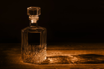 An elegant empty carafe, on a textured wooden table. Decanter in dark style.