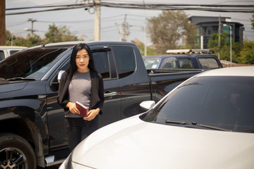 The beautiful Asian woman wearing black suit is posing next to the white car in the sunny day during her working day. 