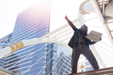 Homeless man is standing in town.He is raising label &ldquo;Help please&rdquo; word.unhappy.poverty,despair,Photo Sympathetic and hope concept.