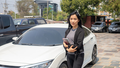 Fototapeta na wymiar The beautiful Asian woman wearing black suit is posing next to the white car in the sunny day during her working day. 