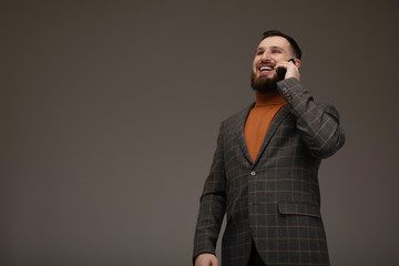 Business and phone talk concept. Man in formal suit has phone conversation. Businessman with happy face isolated on grey background. Men with long beard holds mobile phone.