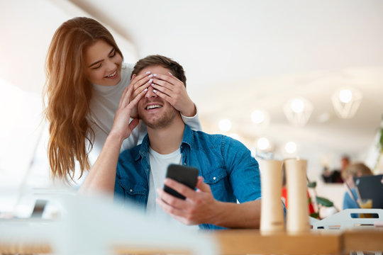 Young Couple Handsome Man And Beautiful Woman Surprising Her Beloved Husband On The Romantic Date At Cafe, Love And Tenderness, Relationships Concept