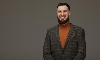 Handsome young bearded man on grey background looking at camera. Portrait of laughing young man.