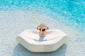 Fototapeta na wymiar Top view of Asian woman wearing sexy white swimsuits with hat leisure and relaxing lounging on white outdoor sofa sun bed lounger at the big swimming pool. Summer vacation concept.