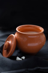 Brown pot with sour cream and a wooden spoon with raisins on a dark background.