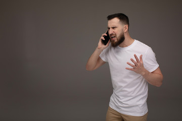 Angry man screaming on the phone isolated on a grey background