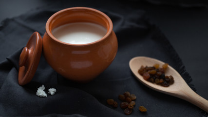 Brown pot with sour cream and a wooden spoon with raisins on a dark background.