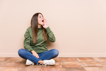 Young caucasian woman sitting on the floor isolated shouting and holding palm near opened mouth.