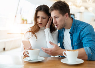 young couple sitting at cafe , handsome man and beautiful woman looking amazed, confused and bewildered hearing bad news, body language concept