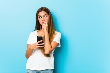 Fototapeta premium Young caucasian woman holding a phone relaxed thinking about something looking at a copy space.