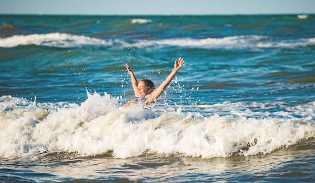 Happy emotional little girl bathes in sea waves