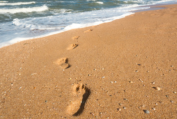 Fototapeta na wymiar Footprints on wet sand leading to sea waves