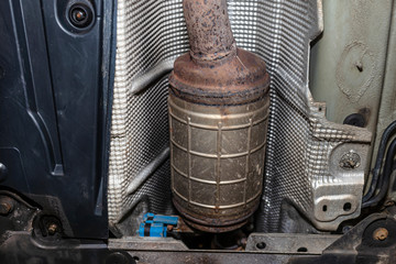 A diesel particulate filter in the exhaust system in a car on a lift in a car workshop, seen from below.