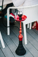 Fototapeta premium Red hookah is standing on wooden floor in interior restaurant. Hookah hot coals on shisha in metal bowl. Stylish oriental shisha. Shisha Smoking Concept. Traditional Asian relaxation.