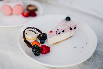 A piece of Birthday pink cake decorated with fresh berries: strawberries, raspberries, currants, blackberries, blueberries and macarons for holiday.