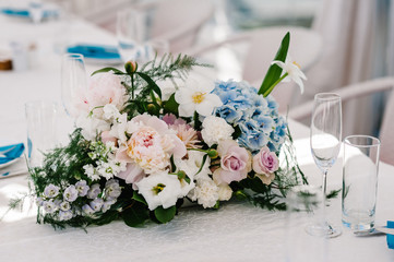 A composition of flowers and greenery is on a festive table at the wedding banquet hall. Close up.