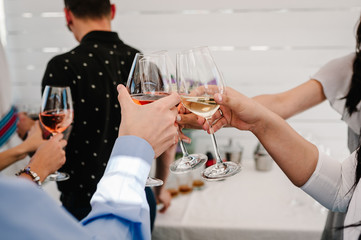 Cheers! People celebrate and hands raise with glasses of wine for toast. Group of man and woman cheering with sparkling champagne in restaurant on party.