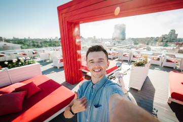 Man on party on terrace at sunlight. Young men on rooftop taking selfie photo on the background of big city and blue sky.