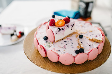 Cut the Birthday pink cake decorated with fresh berries: strawberries, raspberries, currants, blackberries, blueberries and macarons for holiday.