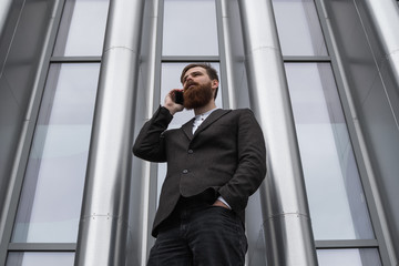 Businessman talking on the phone in financial district. Portrait of a Young urban professional man using smart phone over office building. Business man talking on his smartphone outdoors. Technology.