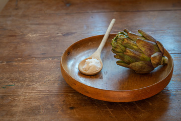 Artichoke in wooden bowl on old table with a spoon full of salt.
