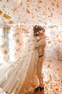 First wedding dance of newlywed. Happy bride and groom dancing under golden confetti in the elegant restaurant with a wonderful light and atmosphere. Romantic moments.