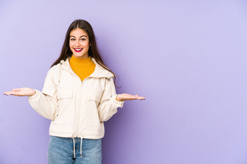 Young caucasian woman isolated on purple background makes scale with arms, feels happy and...
