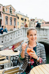 Young female traveler enjoying a glass of spritz in an outdoor cafe in Venice, Italy
