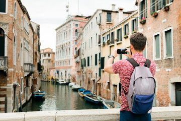 Fototapeta na wymiar Young traveler taking a photo with his smartphone of a canal in Venice, Italy