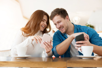 young couple beautiful woman and handsome man sitting at cafe during coffee break, both holding smartphones, technology development concept