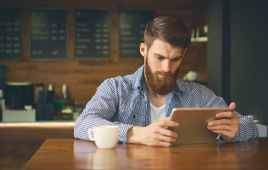 Successful man working in cafe. Freelance and remote job. Coworking space. Bearded man drink coffee work online modern tablet pc. Hipster reading e-mails during Breakfast