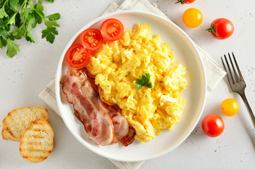Scrambled eggs, fried bacon and tomatoes on plate