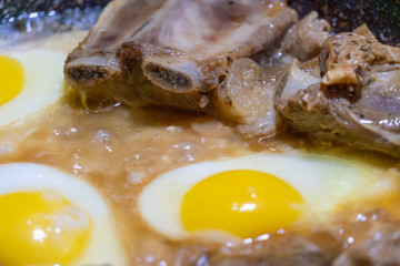 Fried eggs and pieces of meat in a frying pan in sunflower oil close-up. concept of homemade food
