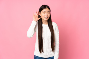 Young asian woman over isolated background listening to something by putting hand on the ear