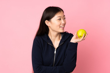 Young asian woman isolated on pink background with an apple and happy