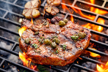 Grilled pork steak pork neck  with addition of capers and aromatic herbs on the grill plate, close up. 