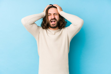 Young long hair man isolated on a blue background laughs joyfully keeping hands on head. Happiness concept.