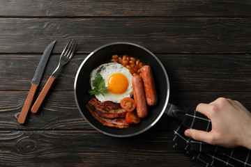 Man hold pan with fried eggs on wooden background, top view