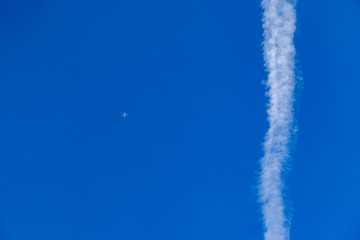 a summer day with blue cloudless sky and an airplane next to a contrail