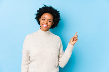 Middle aged african american woman against a blue background isolated smiling cheerfully pointing...