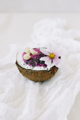 healthy Breakfast berry smoothie with Chia seeds and cashew nuts in a natural coconut plate on a white table with pink flowers