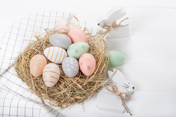 Easter table setting, holiday table home decor idea, flat lay composition with white plates, cutlery, colorful pastel painted Easter eggs, festive decor and fresh spring flowers