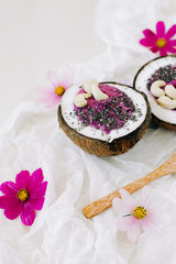 Fototapeta na wymiar healthy Breakfast berry smoothie with Chia seeds and cashew nuts in a natural coconut plate on a white table with pink flowers