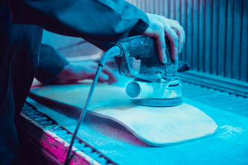 Skater in process of making his own skateboard, longboard - open business concept. Neon lighted studio of creating skateboards. Concept of openspace, craft production, workshop. Polishes, paints.
