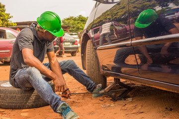 young african man, a professional mechanic, trying to change a car tyre and fix the car