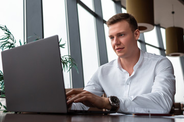 Young businessman wearing a white fashion shirt working hard making a deal in a cafe with a laptop. Freelance and selfemployment concept. Distance dream success job.