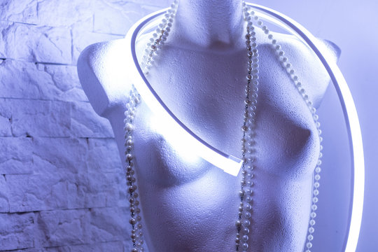 Woman mannequin brest of white color with neon light and necklace on brick background.