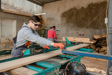 Young man carpenter at the wooden sawmill